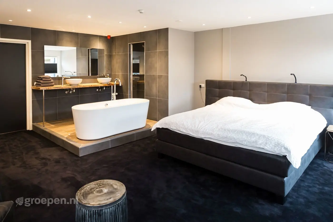 Luxe slaapkamer in groepsaccommodatie met vrijstaand bad en dubbele wastafel.