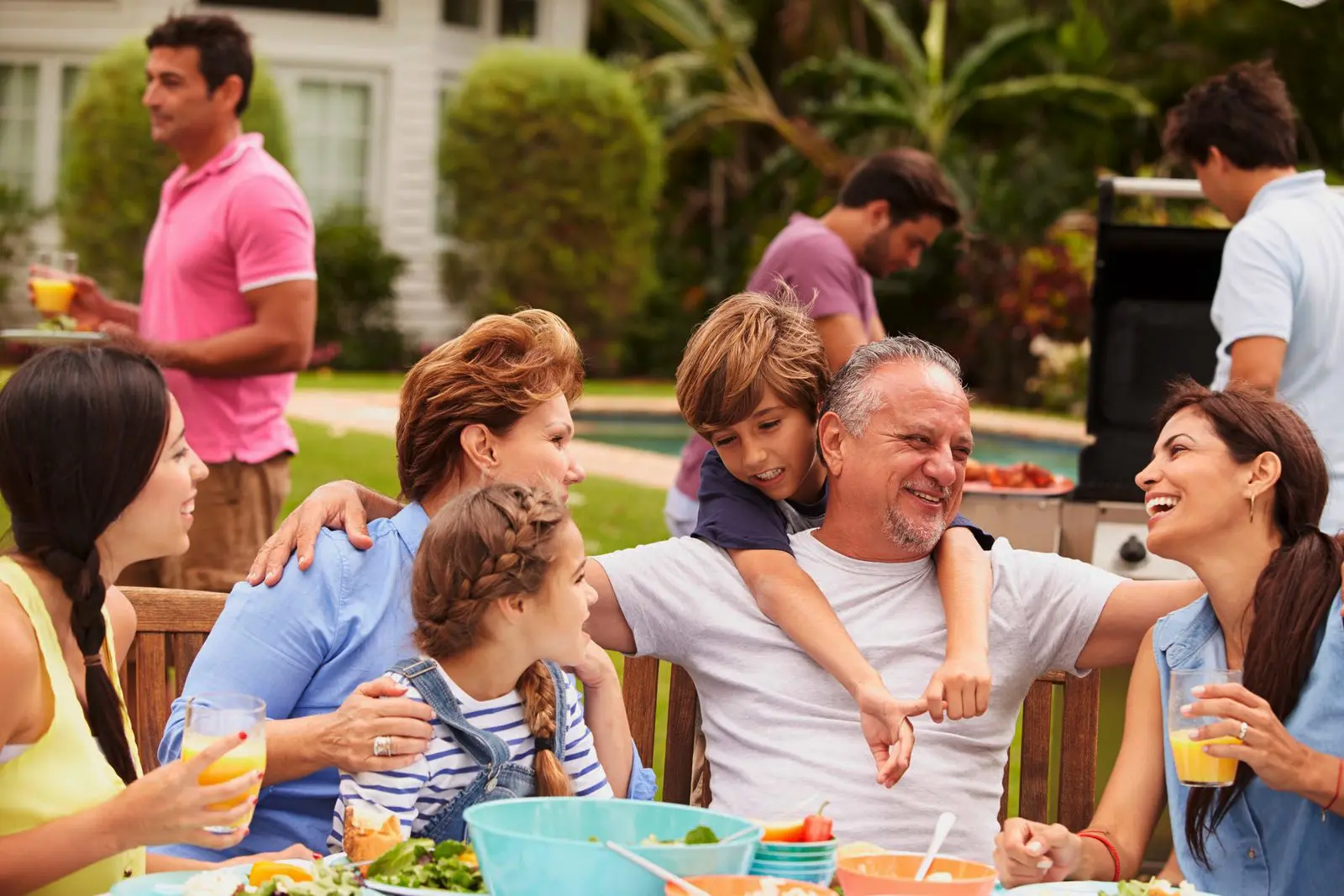 Familie und Freunde genießen ein gemeinsames Grillen im Garten während eines Gruppenurlaubs.